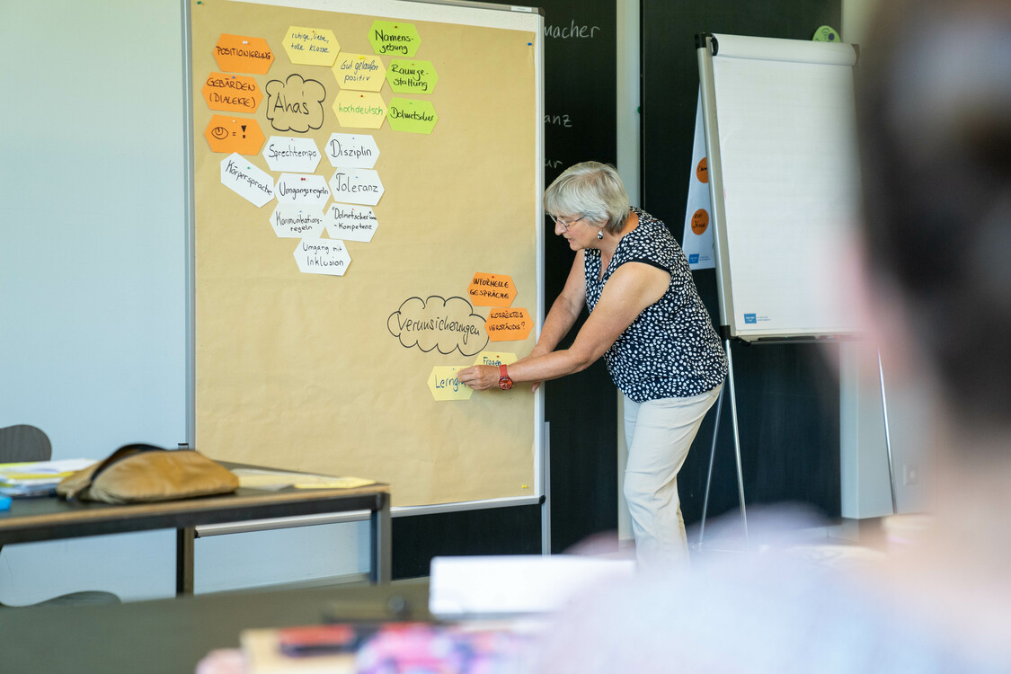 Die Kursleiterin hängt Notizen an die Pinnwand