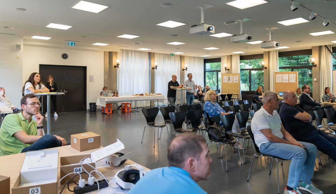 Besucher und Mitarbeiter hören gespannt einer Präsentation zu.