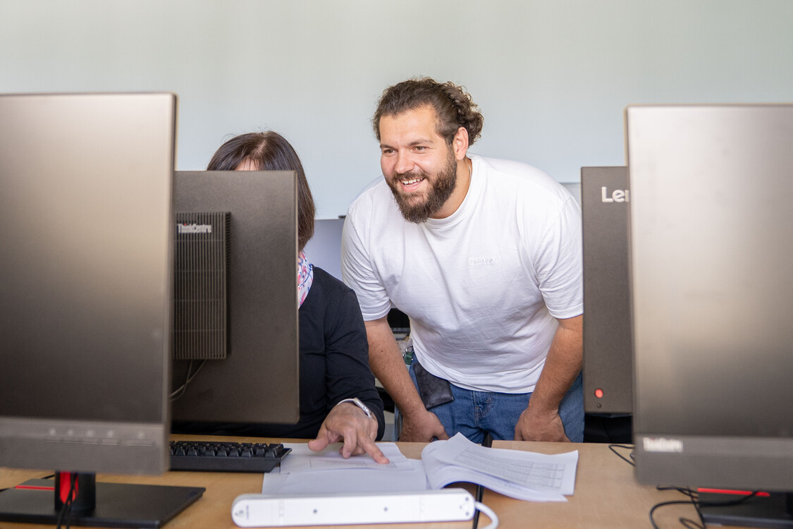 ein RAV-Personalberater schaut einer Kursteilnehmerin bei einer Übung am Computer über die Schulter