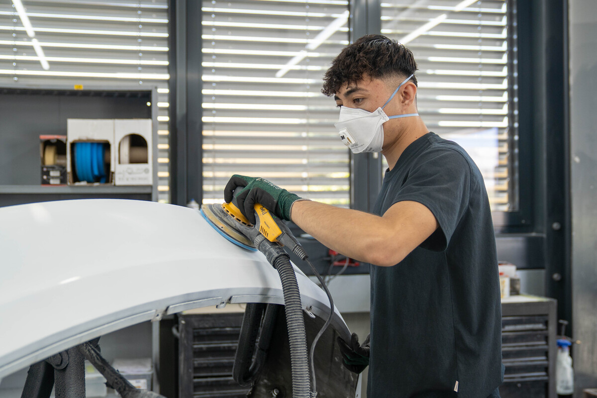 Ein Lernender Carrosserie der Integrationsvorlehre poliert bei der AMAG einen Kotflügen.