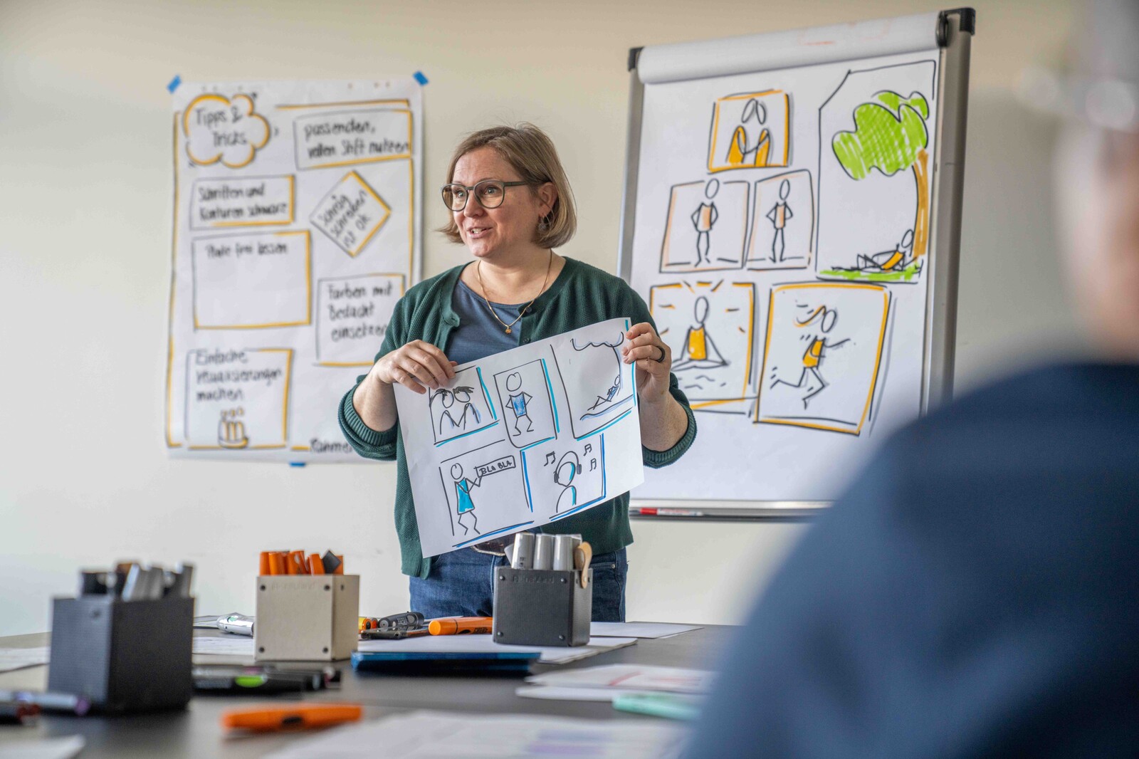 Kursleiterin Katharina E. zeigt vor der Kursgruppe einfache Illustrationen für den Kurs